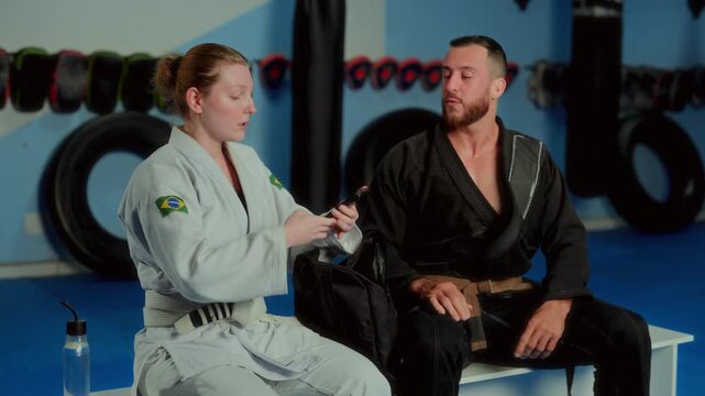 Man and woman Brazilian Jiu-Jitsu athletes sitting and talking in gym and taking selfie