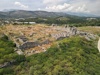Aerial view of scattered Tlos foundations and masonry blocks in Fethiye, Turkiye with houses and greenhouses Traces of streets, courtyards and gates appear among shrubs and grasses after spring rains