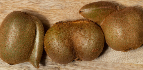 Overhead view of three whole ripe kiwi fruit on bamboo cutting board. Fasciation of fruits.