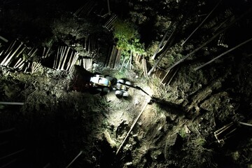 Forestry harvester cutting trees at night in dark forest captured from aerial perspective with...