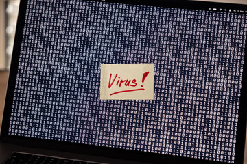 Computer virus, warning message stuck on the screen of a laptop. Binary code, computer crime, system infected, antivirus software.