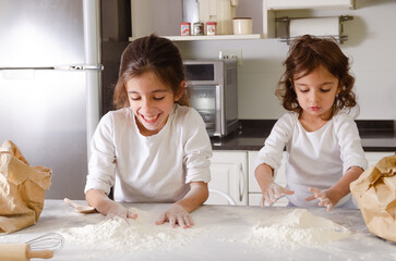 Two happy little girls cooking and preparing the flour for kneading.