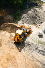 Yellow backhoe loader working near piles of sand and gravel at a construction site
