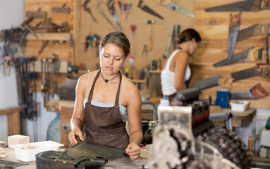Girl is busy in carpentry workshop. Process wooden billet, sand it, applies pattern with cutter....