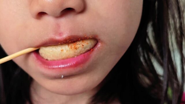 Closeup Woman Bites into Spicy Fish Ball on a Stick Foodie Fun.