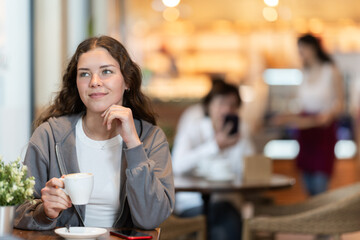 Young European woman enjoys a cup of hot quality coffee made from Arabica beans. Woman enjoys drinking cappuccino in a coffee shop