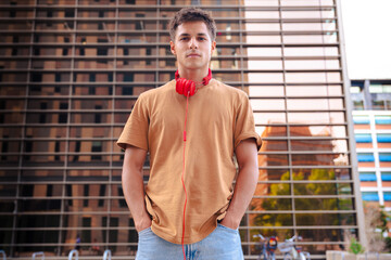 Portrait of a young man smiling warmly at the camera while wearing red headphones around his neck,...