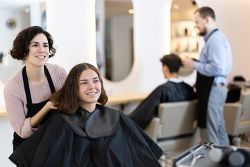 Adult female hairdresser stylist discussing haircut with young female client in beauty salon