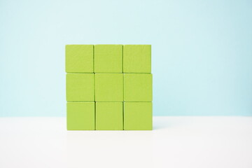 Minimalist arrangement of green wooden cubes on a white surface against a blue background. It can be used to explain and clarify various concepts.