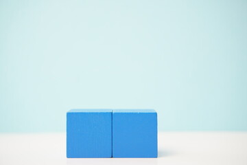 Close-up of two blue wooden blocks on a white surface against a soft blue background. It can be used to explain and clarify various concepts.