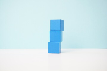 Stack of three blue wooden cubes on a white surface with a light blue background. strategy, business, economy and educational concepts