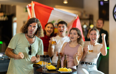Happy man and woman sport fans holding flag of Peru, celebrating and drinking alcoholic drinks in...