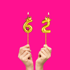 Birthday on a fuchsia background with the number 62 - Hands holding number-shaped candles