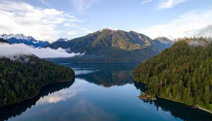 Naklejka premium Serene mountain lake reflecting a misty mountain range, surrounded by lush forests.