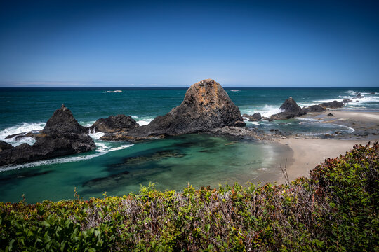 Peaceful Coastal Scene: Rocky Shore with Jagged Outcrops, Clear Blue Waters, and Distant Landscape
