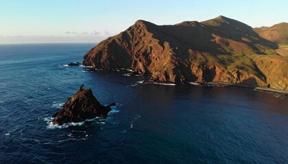 Fototapeta premium Dramatic coastal cliffs and a solitary rock formation rise from the deep blue ocean under a clear sky.