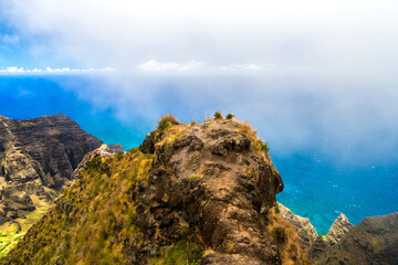 Dramatic aerial view of the rugged Na Pali Coast on Kauai, Hawaii, with steep cliffs dropping into the vibrant blue Pacific Ocean.