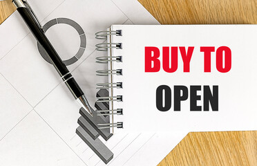 Notepad with buy to open text on wooden desk with black pen and business charts