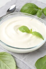 Tasty yoghurt with basil in bowl on table, closeup
