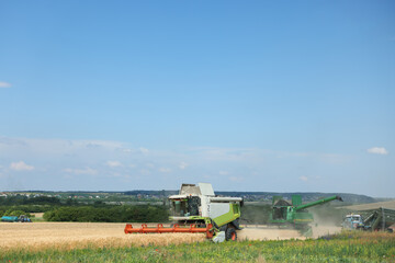 Modern combine harvesters and tractor working in wheat field