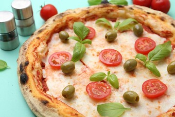Delicious pizza with tomatoes, basil and olives on turquoise background, closeup