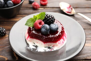 Delicious panna cotta with berries, jam and mint on wooden table, closeup