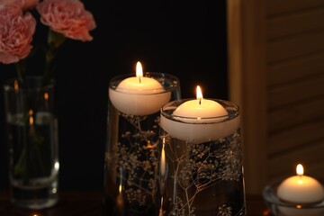 Burning candles and flowers in glasses of water on black background, closeup