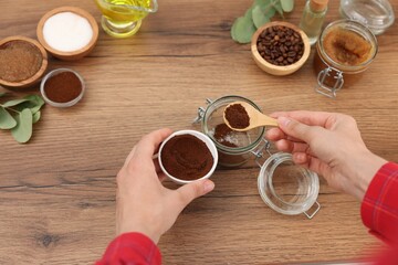 Making natural scrub. Woman adding coffee into jar at wooden table, top view