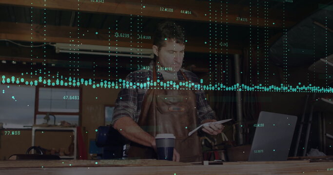 Reviewing leather-aproned woodworker consulting tablet at workshop bench, with laptop, data overlay