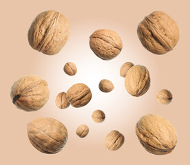 Walnuts in shell swirling in air against dark beige background