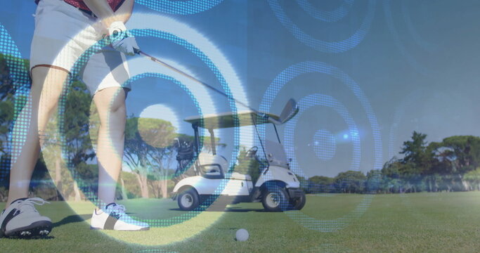 Swinging male golfer gripping club and targeting teed ball on fairway, with golf cart, copy space