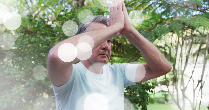 Meditating mature man wearing blue T-shirt practicing yoga in backyard, dreamy sunlight overlay - Powered by Adobe