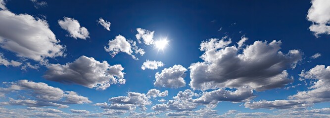 A vast expanse of a partly cloudy blue sky, with scattered cumulus clouds and a bright sun