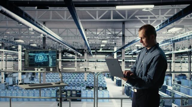 Data center engineer monitors machine learning process with laptop, reviewing operational metrics. IT specialist reviews neural networks reports during inspection to verify ongoing stability, camera A