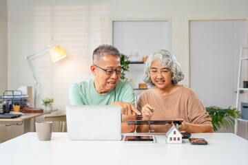 Happy senior couple using laptop counting taxes refund receipts to save money at home. Old man and woman paying bills online planning financial budget savings calculating payment at desk.