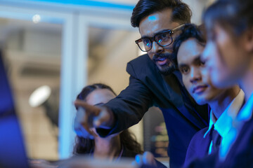 An Indian business manager leads his diverse team, analyzing critical market data on a screen....