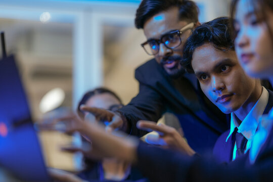 An Indian business manager leads his diverse team, analyzing critical market data on a screen. Intense focus on financial strategy and corporate decision making in a modern office.