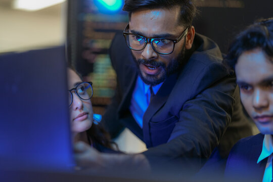 A senior AI architect mentors a diverse team as they debug a complex neural network. Intense, focused collaboration on developing the future of Artificial General Intelligence (AGI). - Powered by Adobe