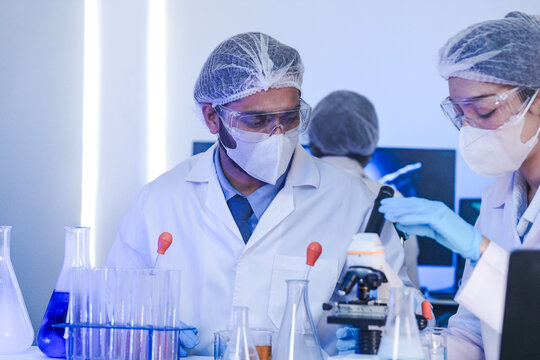 A team of diverse scientists discusses experimental results in a high-tech lab. A male researcher presents a sample in a test tube while colleagues analyze data for a new discovery.