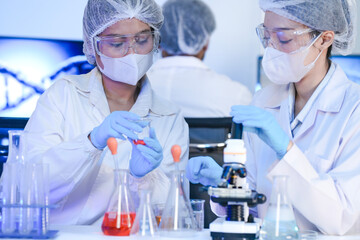 A diverse team of scientists collaborates in a high-tech biotech lab. A senior researcher mentors...