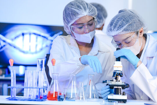 A diverse team of scientists collaborates in a high-tech biotech lab. A senior researcher mentors his colleague as she carefully pipettes a solution into a test tube for an experiment. - Powered by Adobe