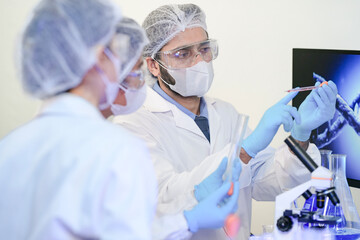 A diverse team of scientists collaborates in a high-tech biotech lab. A senior researcher mentors...