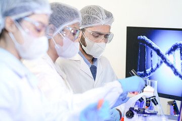 A diverse team of scientists collaborates in a high-tech biotech lab. A senior researcher mentors...