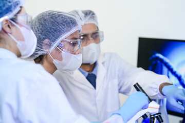 A diverse team of scientists collaborates in a high-tech biotech lab. A senior researcher mentors...