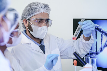 A diverse team of scientists collaborates in a high-tech biotech lab. A senior researcher mentors...