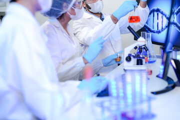 A diverse team of scientists collaborates in a high-tech biotech lab. A senior researcher mentors...