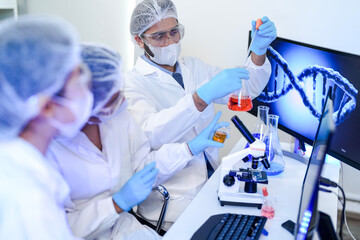 A diverse team of scientists collaborates in a high-tech biotech lab. A senior researcher mentors...