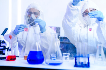 A diverse team of scientists collaborates in a high-tech biotech lab. A senior researcher mentors...