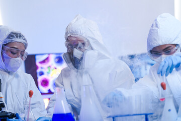 A diverse team of scientists collaborates in a high-tech biotech lab. A senior researcher mentors...