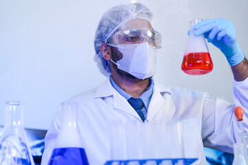A focused scientist in full protective gear meticulously compares two different chemical solutions...